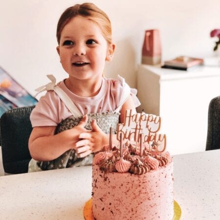 3 year old birthday girl with pink happy birthday cake and candles